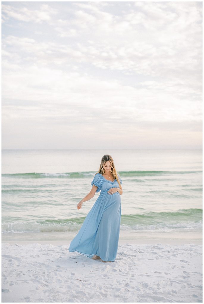 Pregnant mother in blue dress lets her dress blow in the wind during her beach maternity session