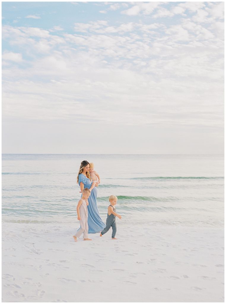 Mother walks with her three young boys on the beach during her maternity session