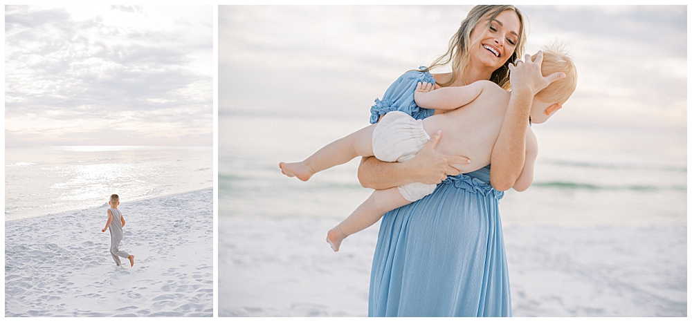 Mother wearing a blue dress stands on the beach holding her young son and laughing during her maternity session