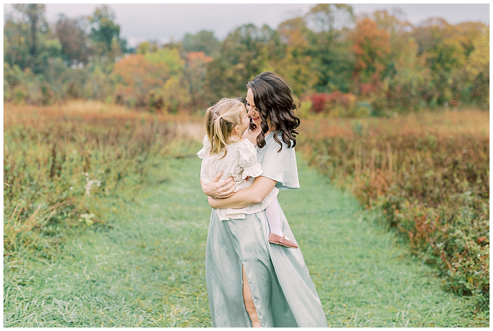 Mother gives her toddler daughter a nose nuzzle while carrying her during their family session at the Howard County Conservancy