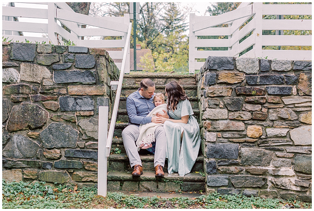 Mother, father, and young daughter sit on stone steps at the Howard County Conservancy
