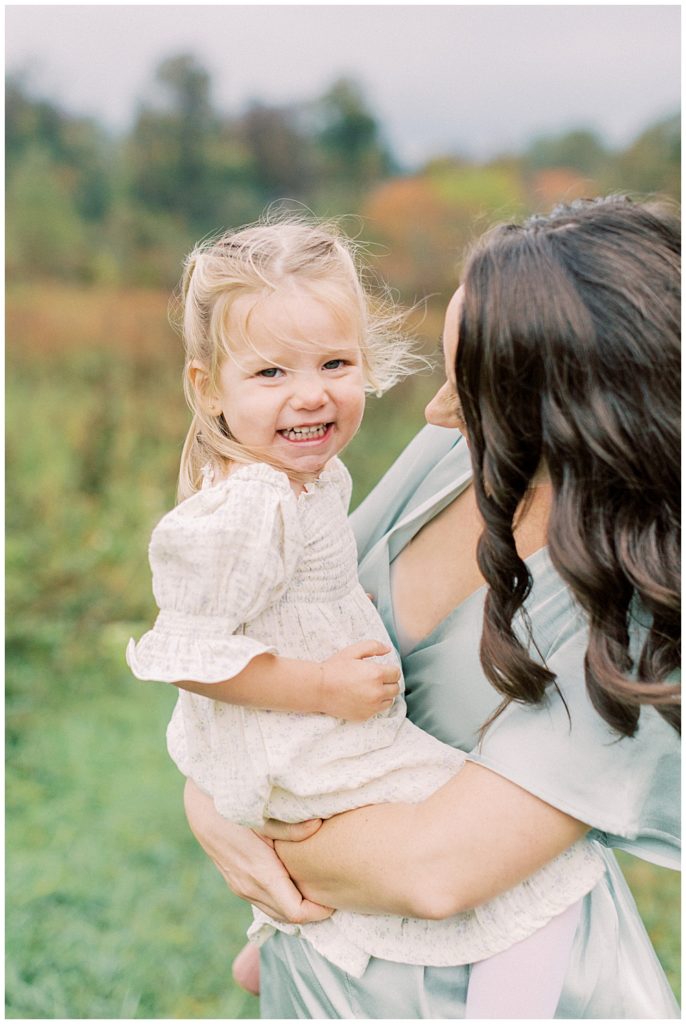 Little girl smiles at the camera while her mother carries her