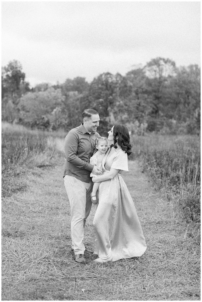 Black and white portrait of mother, father, and young daughter standing in a clearing in the howard County Conservancy