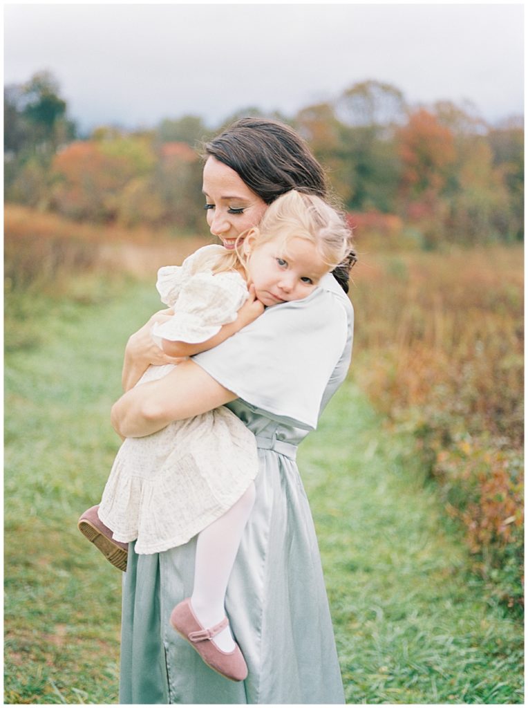 Mother holds her daughter up against her during their fall family photos at the Howard County Conservancy