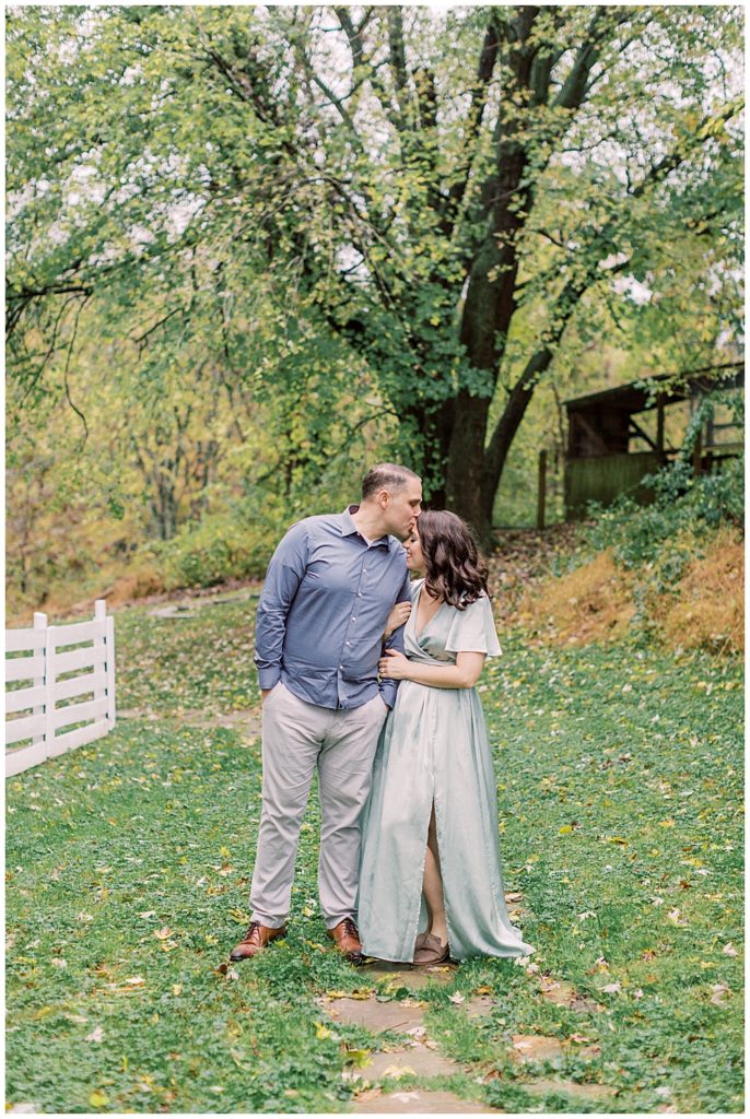 Husband leans in and kisses his wife on the forehead during their family photo session at the Howard County Conservancy