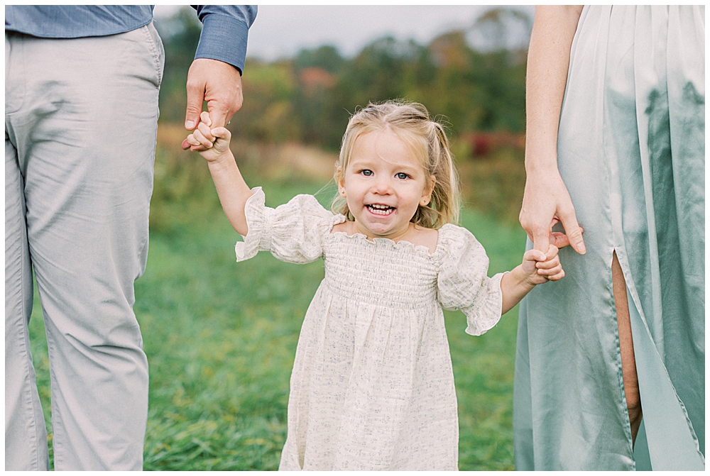 Little girl smiles as she holds her mother and father's hands at the Howard County Conservancy