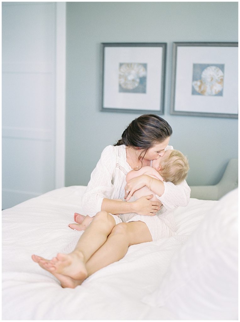 A mother cradles her infant close to her while sitting on a bed during her lifestyle family session in Bethesda, Maryland
