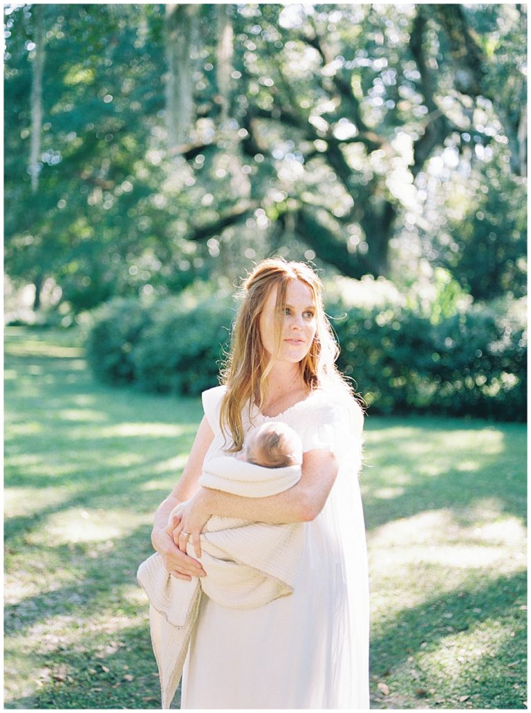 A red haired mother holds her newborn and looks off into the distance during her outdoor newborn session