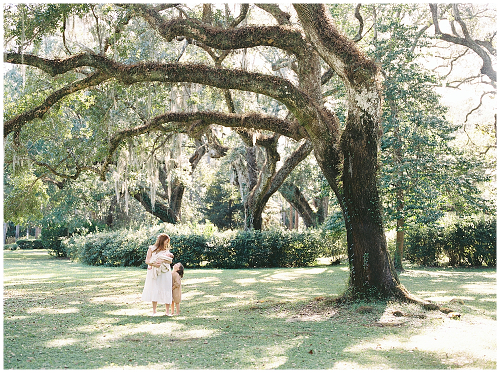 A mother and daughter walk together in a park under a large tree with Spanish moss