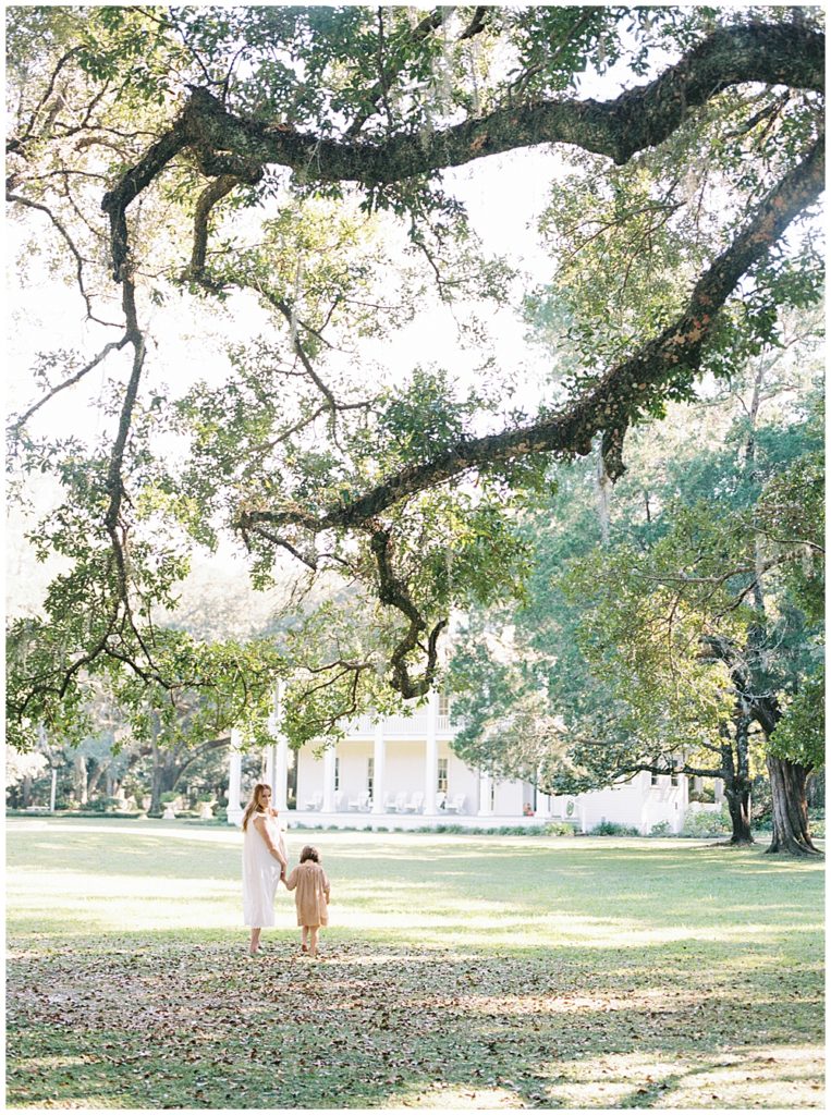 Mother and daughter walk under a large tree with Spanish moss during their outdoor newborn session