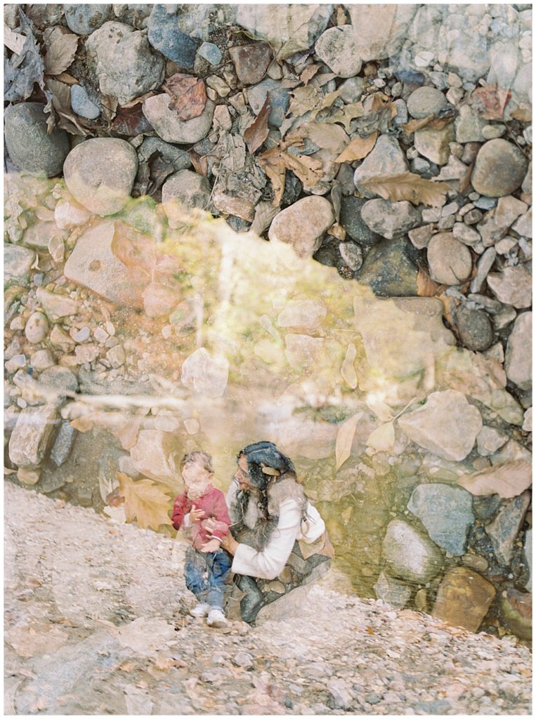 A double exposure of a mother crouched down with her son and rocks by the creek