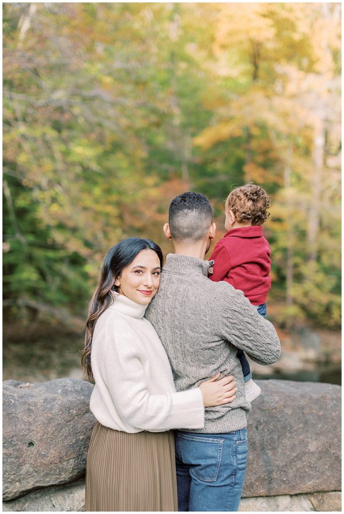 A mother hugs her husband who is holding their son while standing on Boulder Bridge in Rock Creek Park in DC