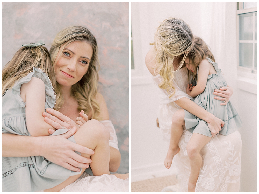 A studio motherhood session with a mother in a white dress and her young daughter in a green dress cuddling together