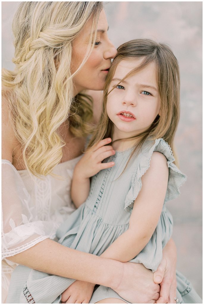 A mother kisses the side of her daughter's head during their studio motherhood session