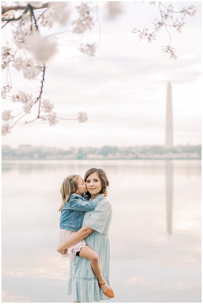 Mother holds her daughter by the Tidal Basin cherry blossoms while her daughter kisses her cheek