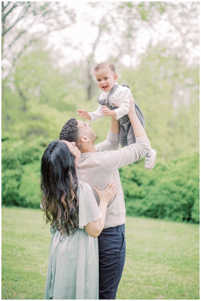 Parents hold up their toddler son in the air while he smiles during their Elegant Family Photos at Salubria