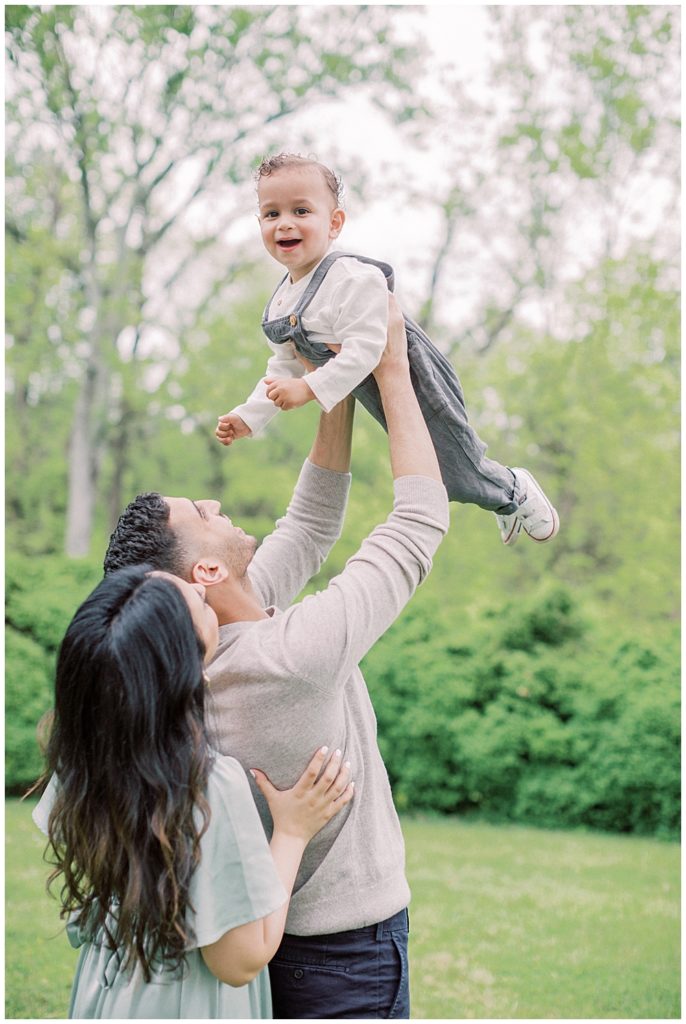 Parents hold up their toddler son in the air while he smiles