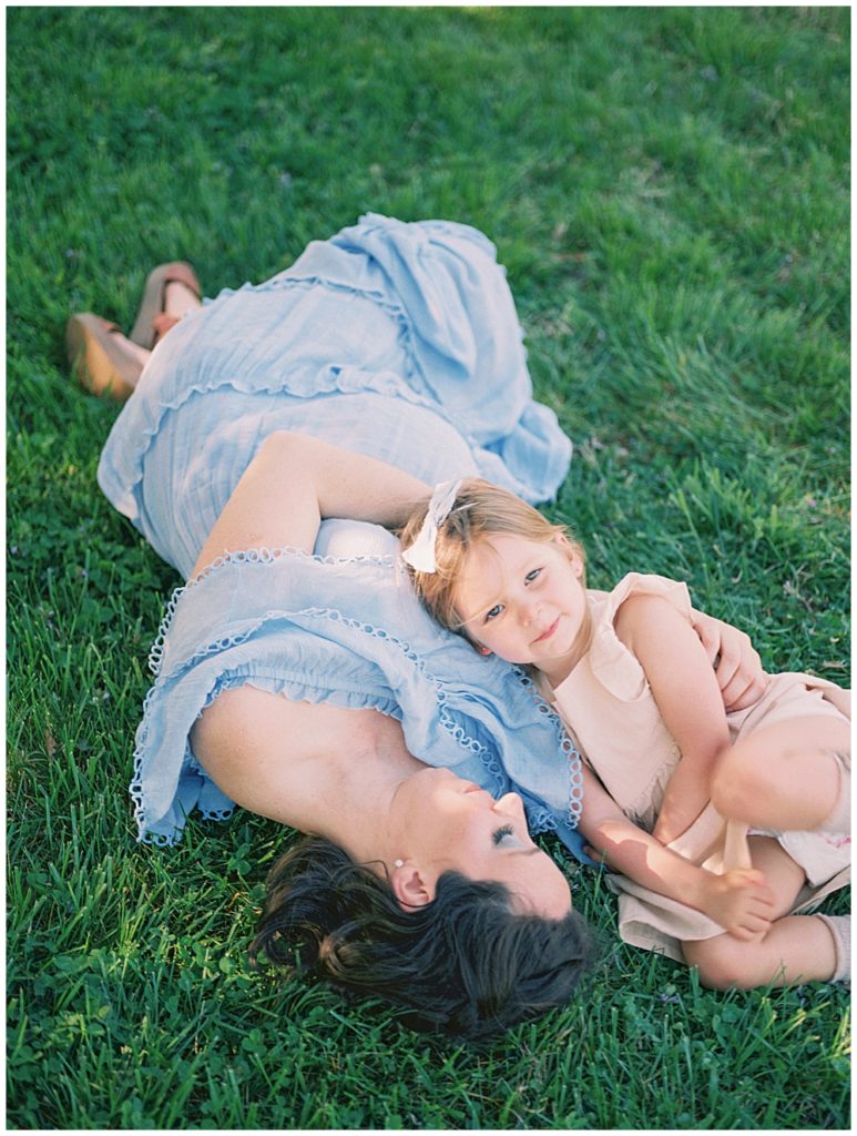 A little girl lays on her mother in the grass during a maternity session at the National Arboretum