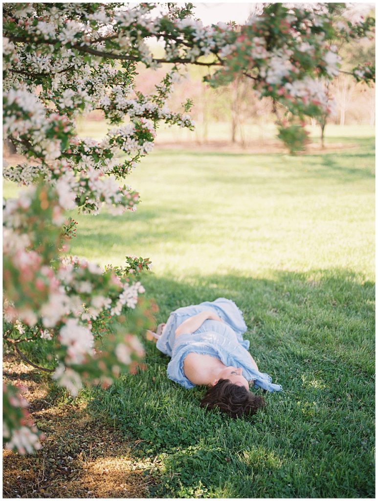 An expecting mother in a blue dress lays in the grass by a cherry tree at the National Arboretum