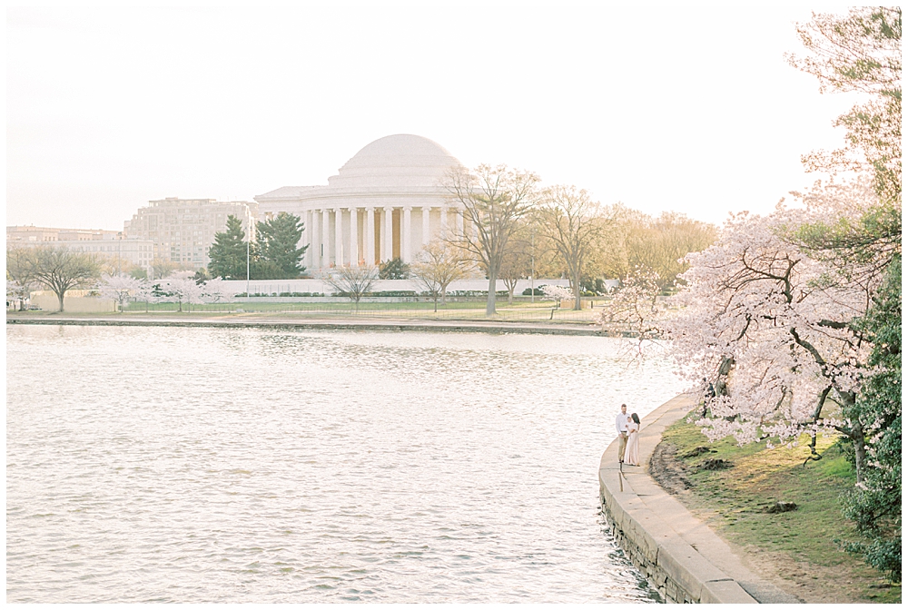 Mother, father, and baby stand along the Tidal Basin in front of the Jefferson Memorial during sunrise and peak cherry blossom bloom.