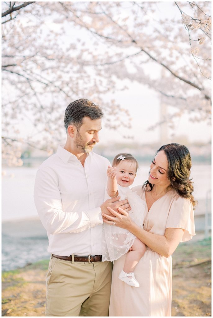 A father and mother hold and smile at their one year old daughter at the DC cherry blossoms