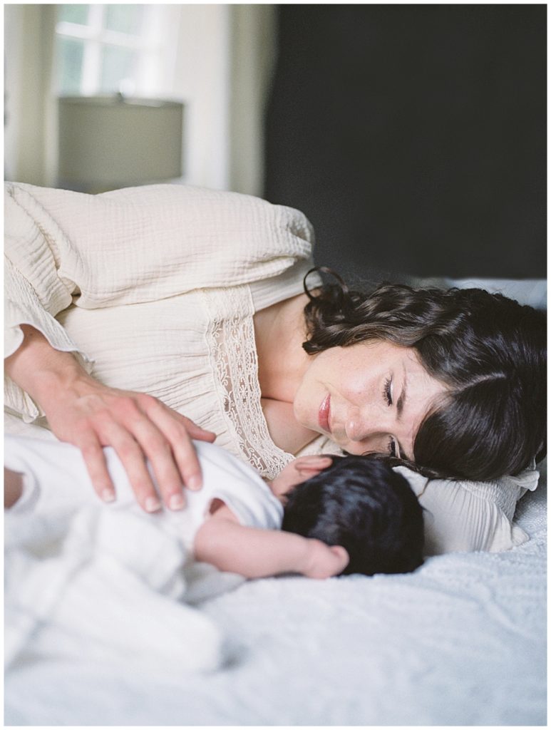 A brown-haired mother lays down in bed with her baby during her Baltimore newborn session.