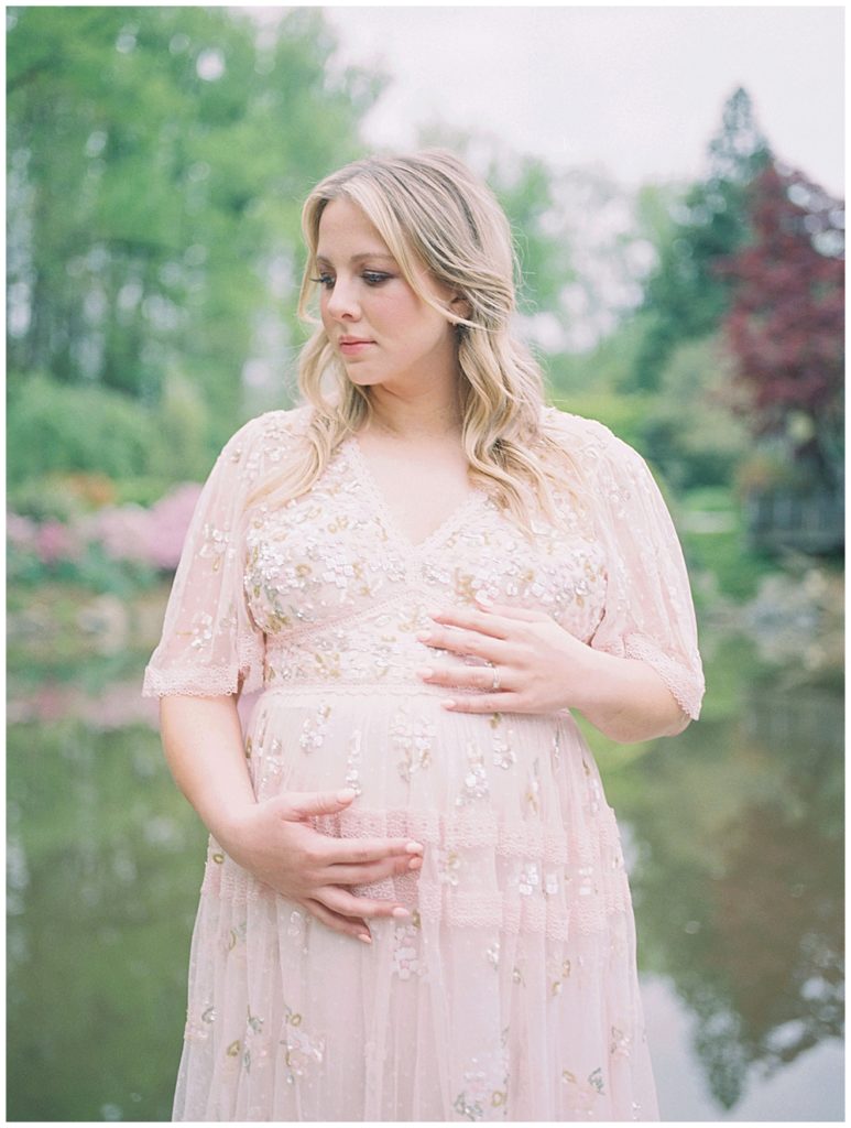 Blonde mother in pink sequin Needle & Thread gown stands in front of pond at Brookside Gardens