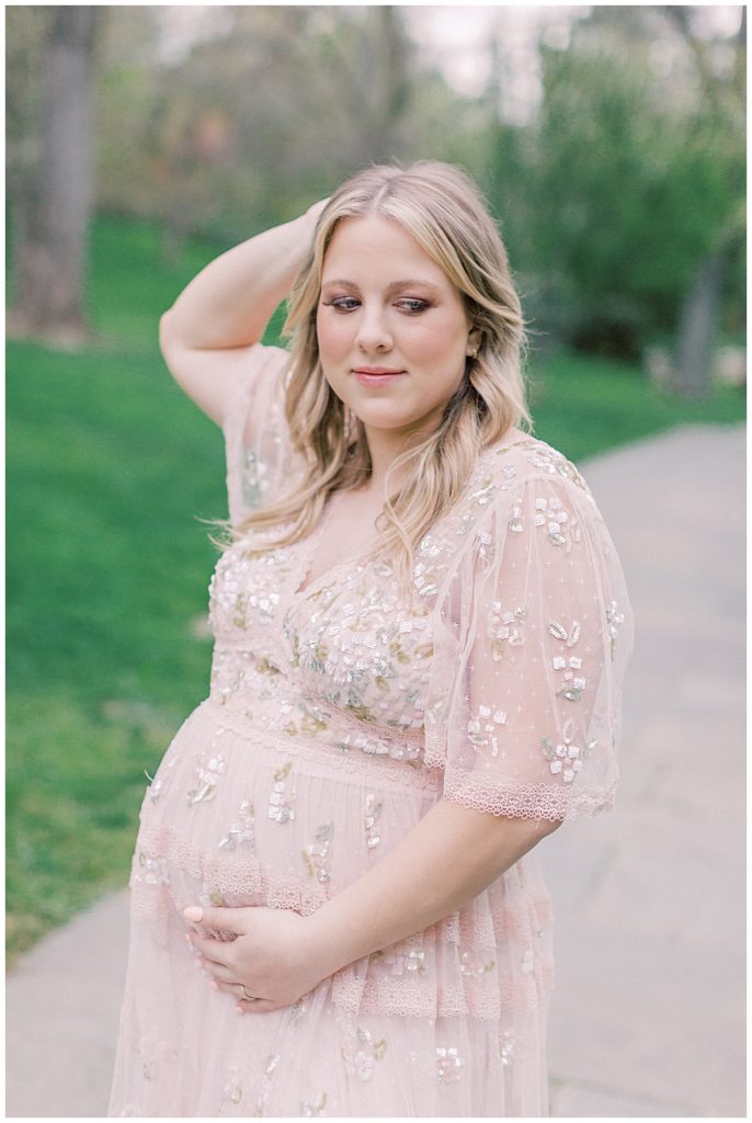 A blonde mother-to-be in a pink Needle & Thread gown during her garden maternity session.