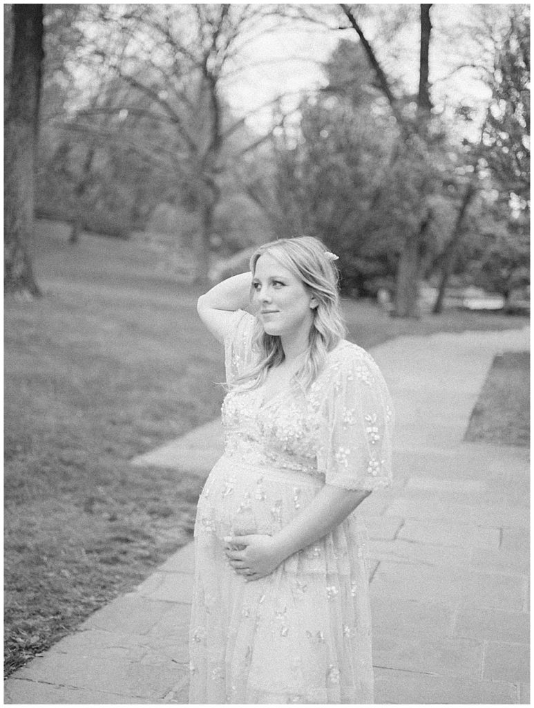 A black and white image of a mother cradling her pregnant belly with one hand and one hand behind her head.
