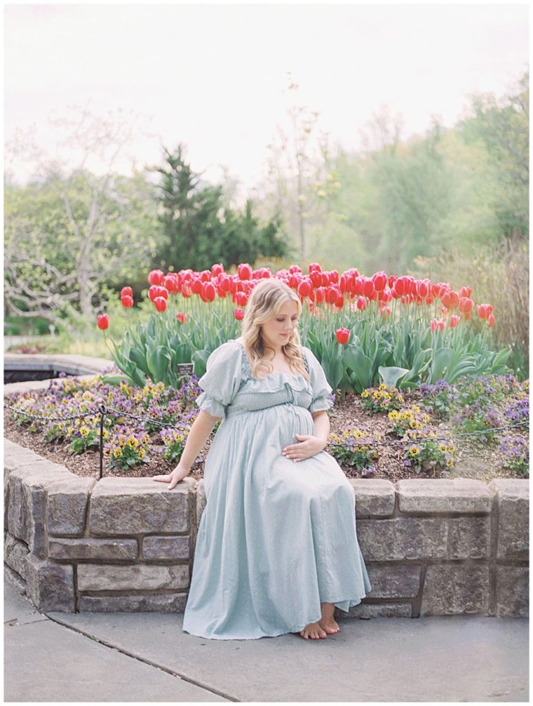 An expecting mother in a green dress sits in front of red tulips at Brookside Gardens.