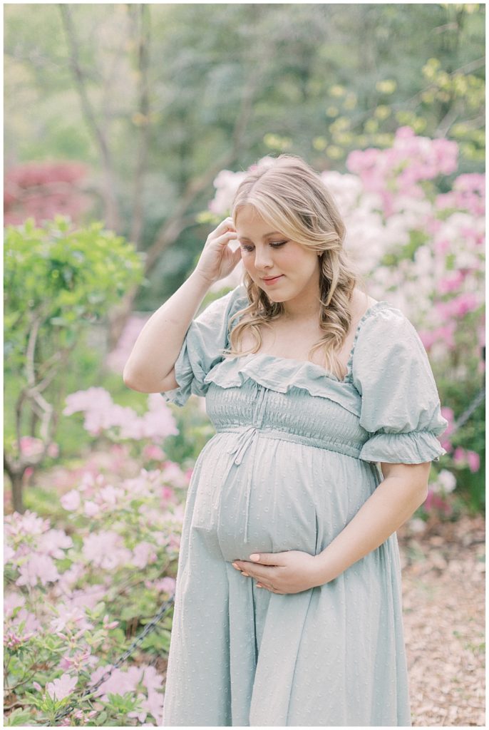 An expecting mother with blonde hair cradles her belly with one hand and brushes hair away with the other.