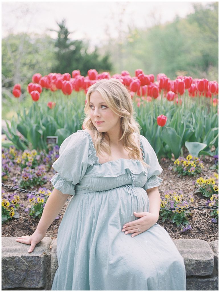 A pregnant mother sits in front of red tulips at Brookside Gardens.
