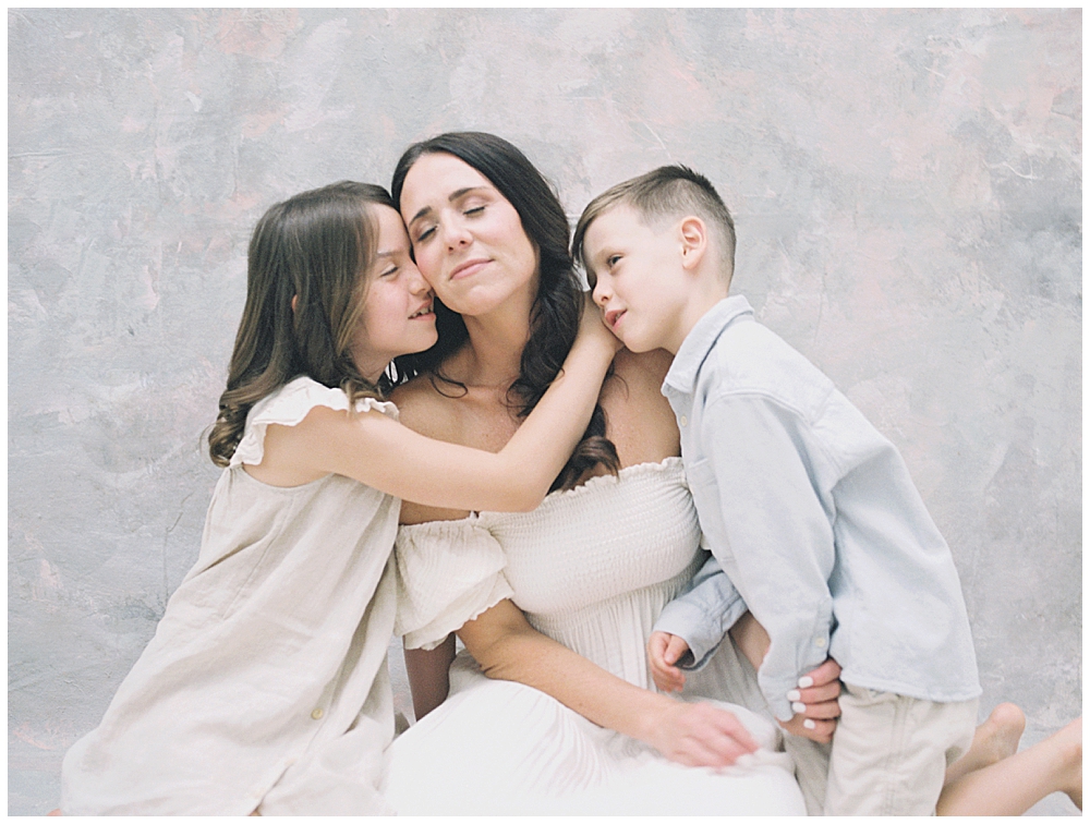 A mother closes her eyes while her daughter and son embrace her