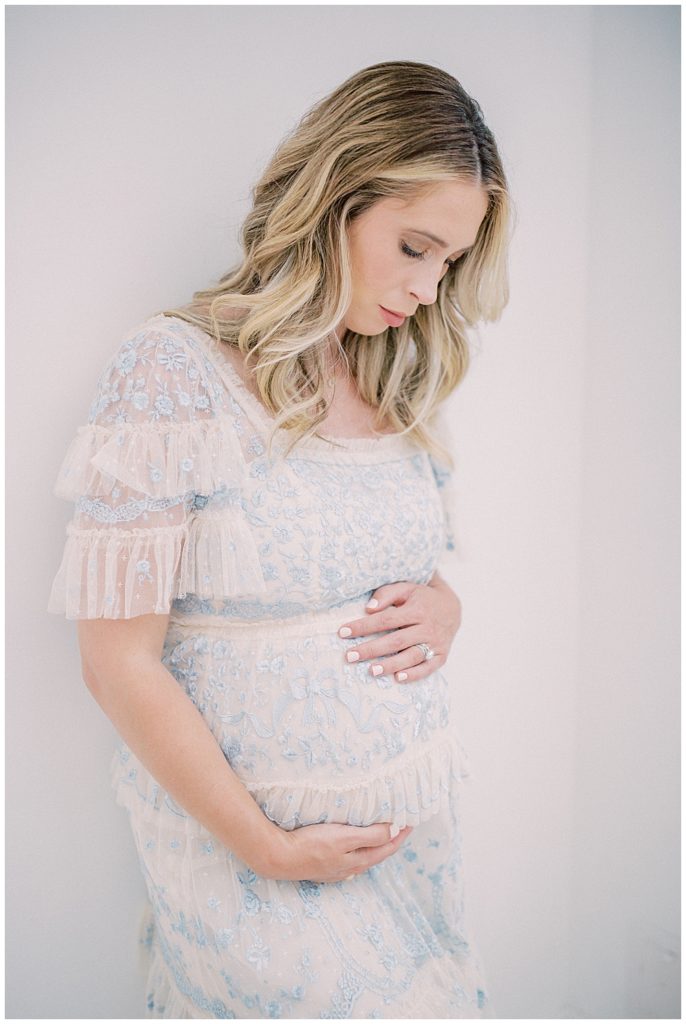 A blonde, pregnant mother places one hand below her belly and one on top while looking down at her baby bump