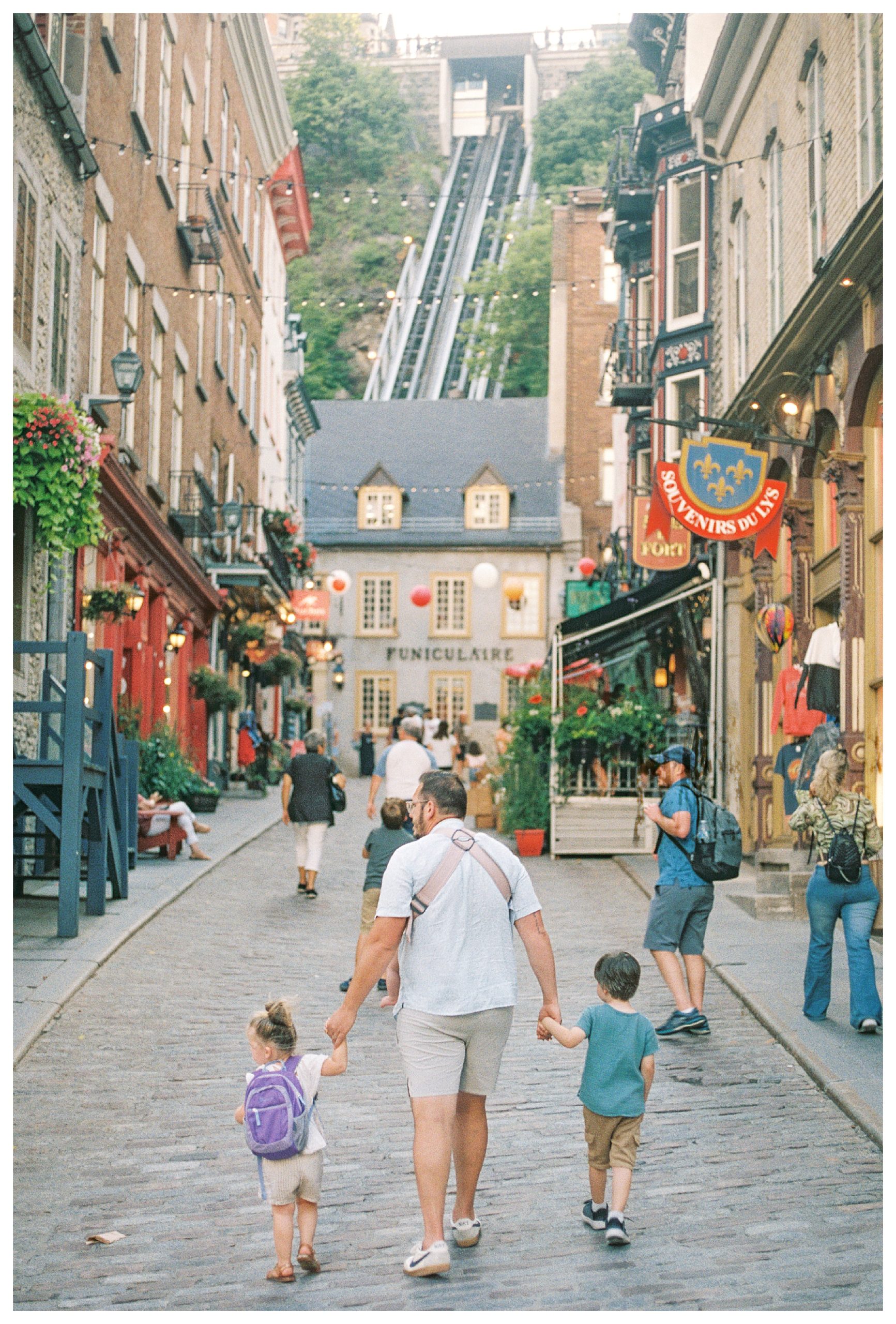 Father walks along street in Old Quebec towards the furniculaire with his two young children.