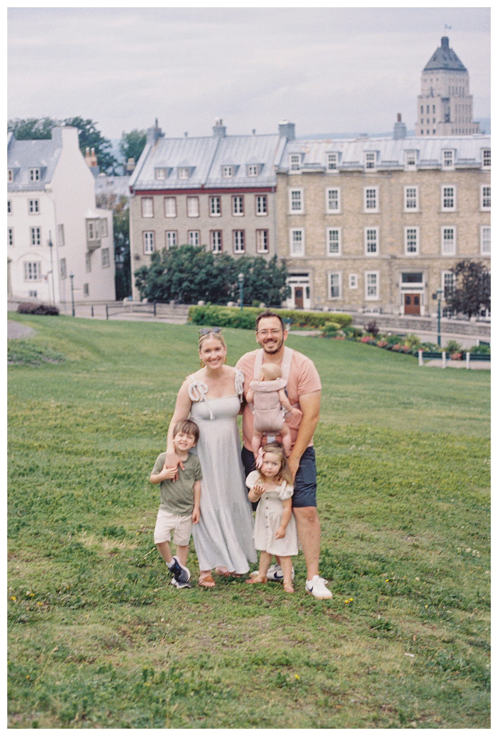 Family of five stands together in Quebec City grassy field.