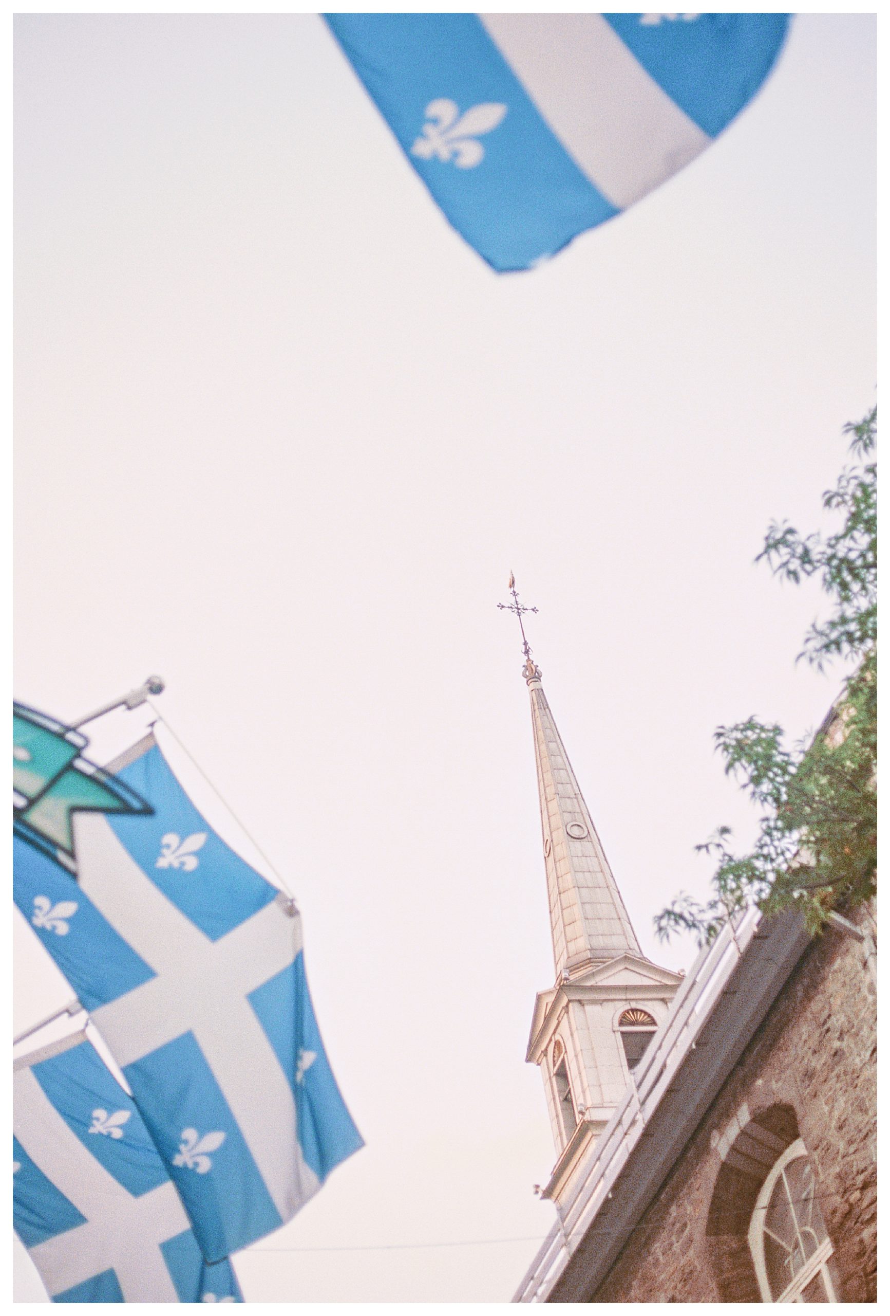 The Montreal flag waves in front of a church steeple in Quebec City.