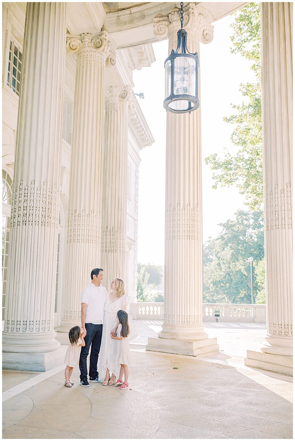 Mother, father, and their two daughters stand under the columns at the DAR Constitution Hall during their family photo session.