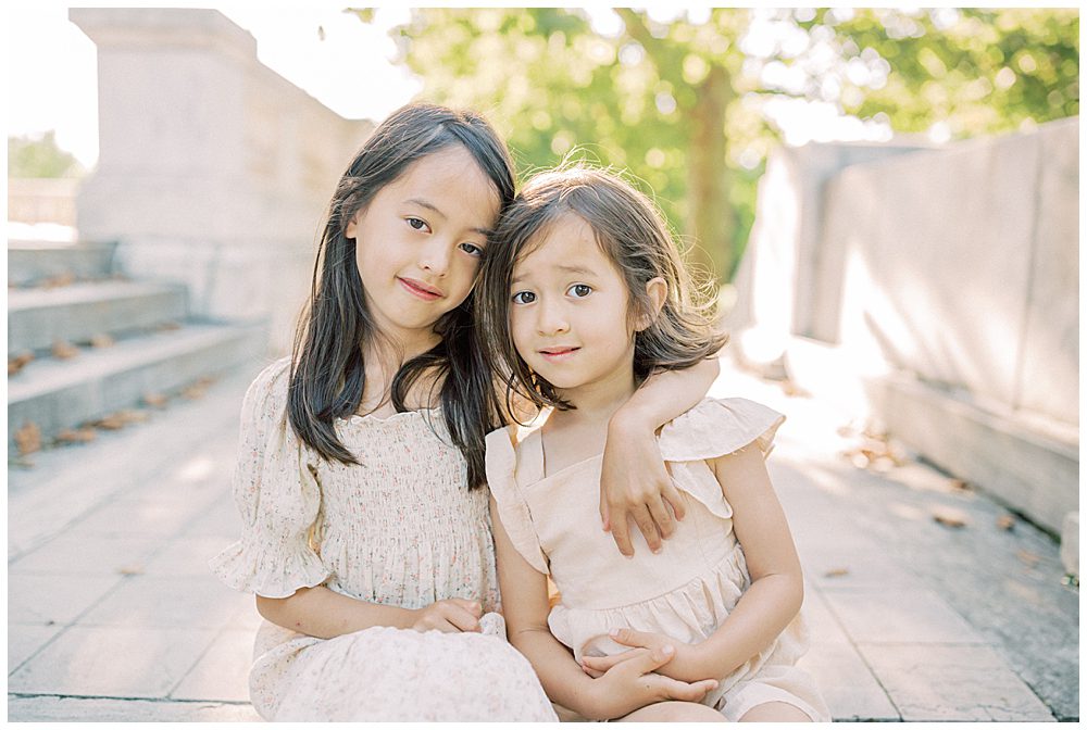 Two sisters sit together on the steps of DAR Constitution Hall during their family photo session.