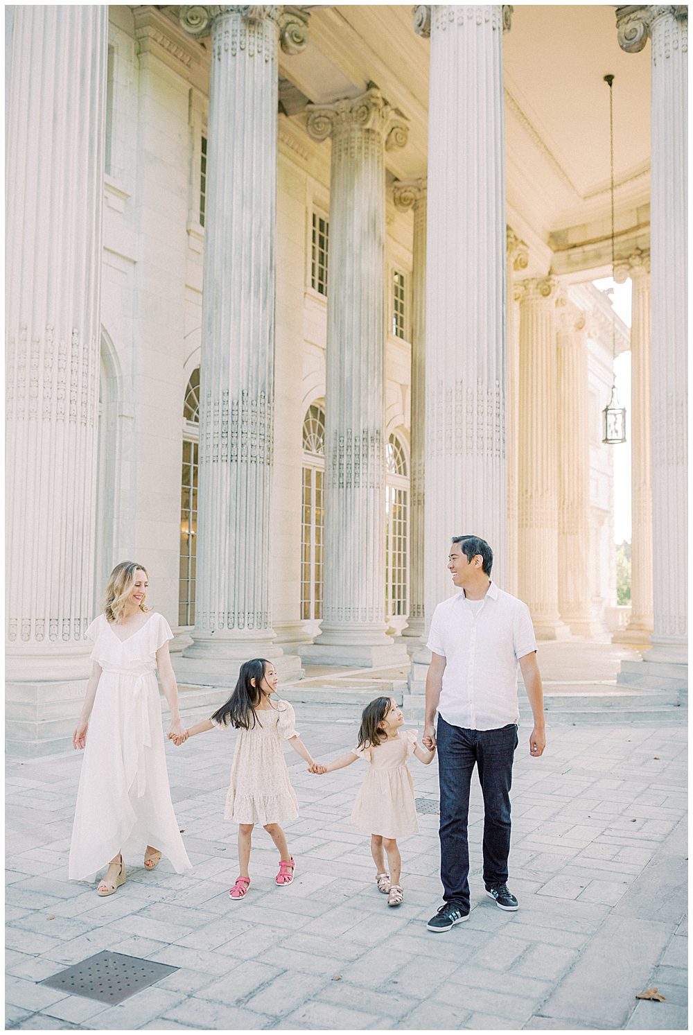 Mother, father, and two young girls walk together in front of the columns at DAR Constitution Hall during their DAR Constitution Hall Family Session in DC.