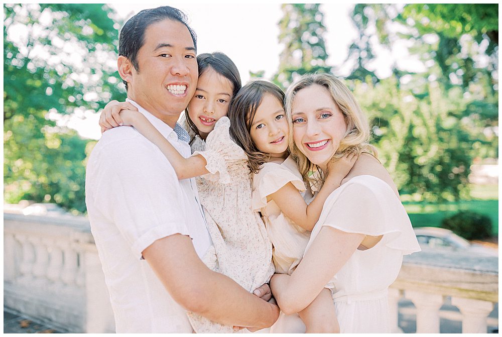 Blonde mother, Asian husband, and two young girls stand together at the DAR Constitution Hall during their family photo session.