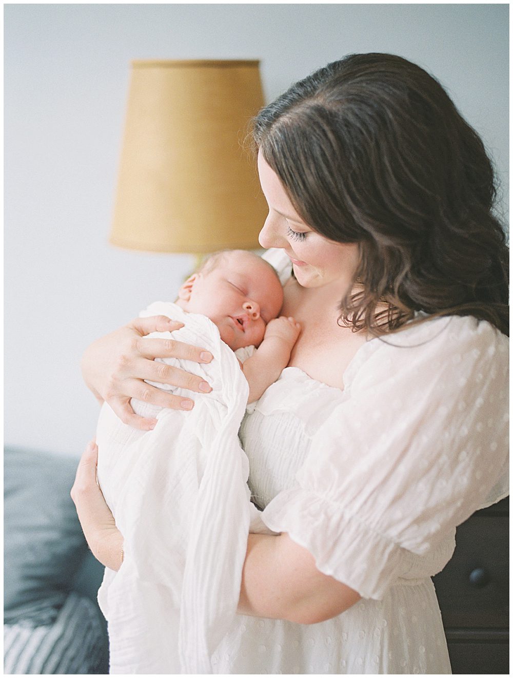 Brown-haired mom in white dress holds newborn baby up to her chest and smiles at him during her Capital Hill Newborn Session.