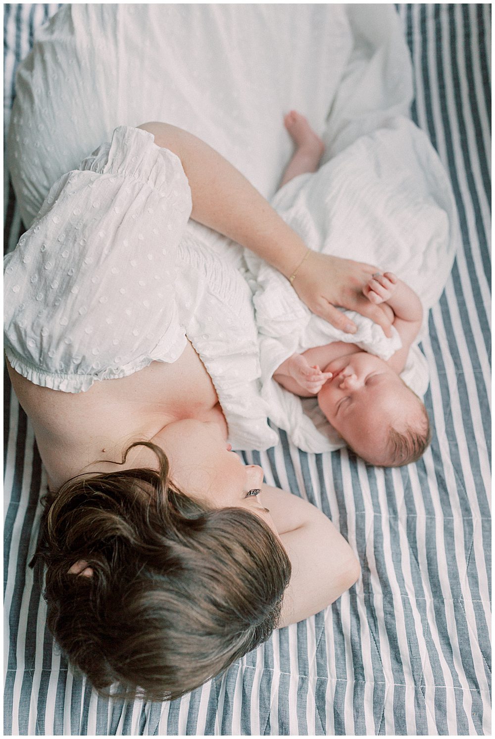 New mom lays down on blue and white striped bed next to her newborn baby during their Capital Hill Newborn Session