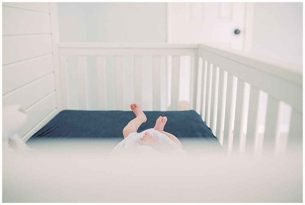 Baby toes stick up from outside a white and navy crib.