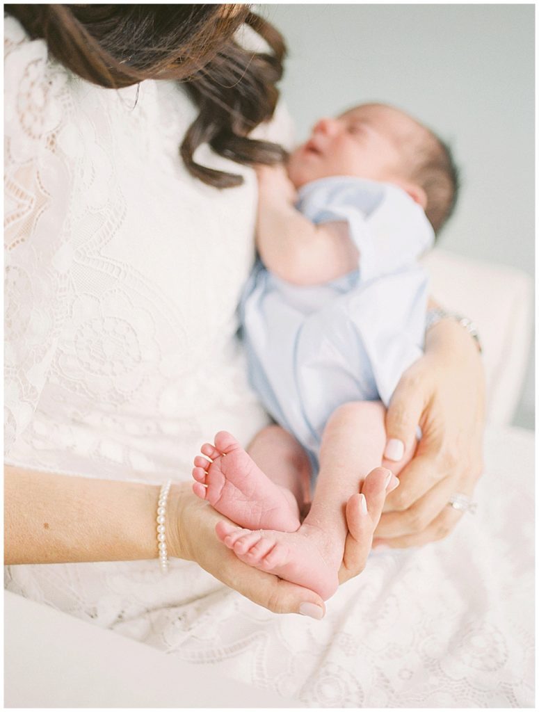 Baby feet of a newborn in blue outfit held by his mother.
