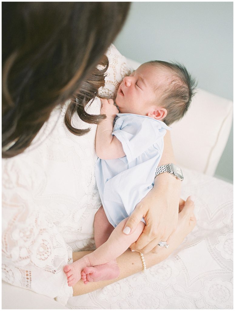Newborn baby in heirloom blue bubble outfit held by his mother.