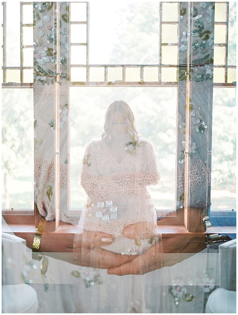 A double exposure of pregnant mom sitting in a window and her hands holding her belly