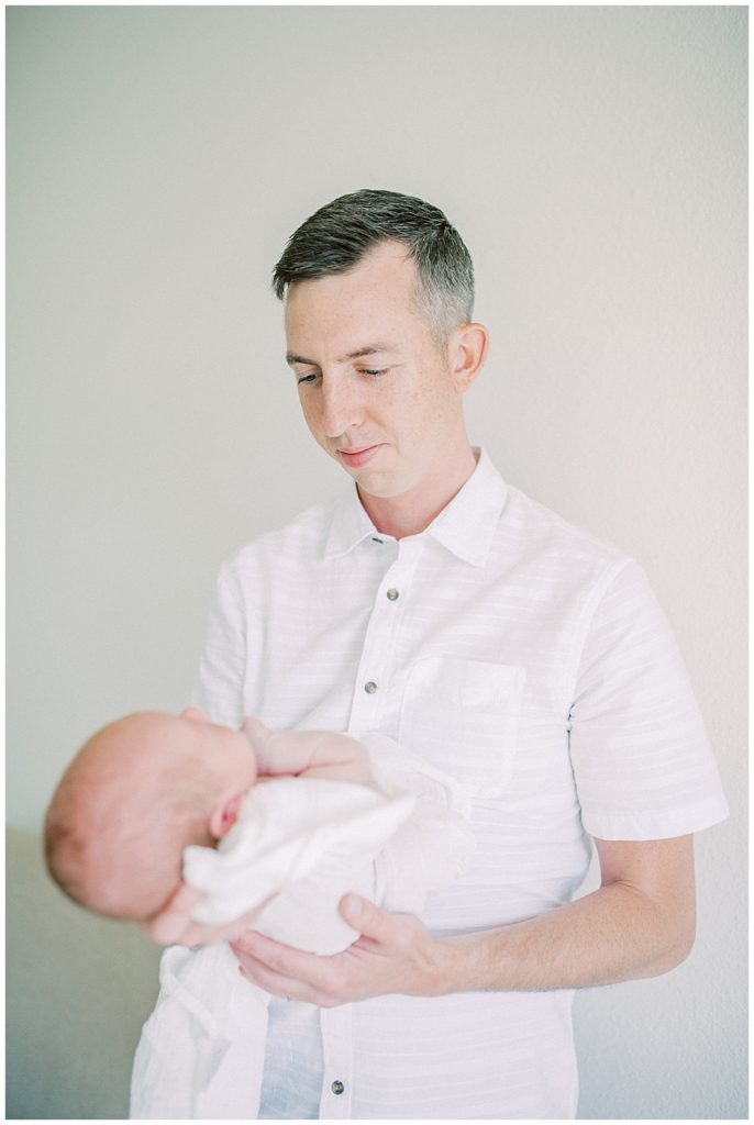 Father holds his newborn baby in front of him, looking down at him.