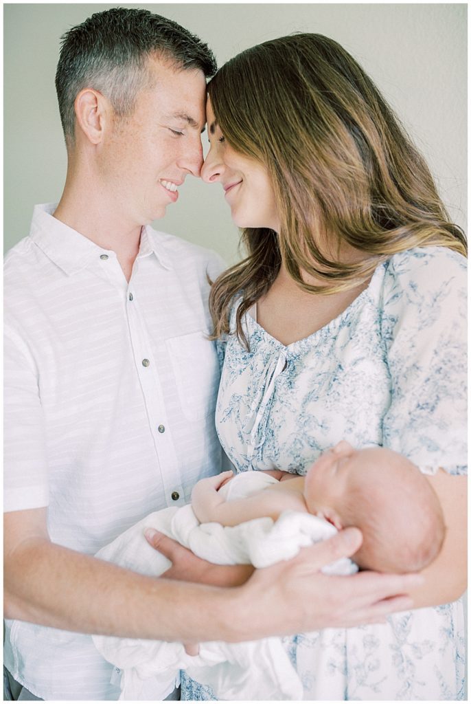 Father and mother smile and lean in together while holding their baby during their Joint Base Andrews newborn session.