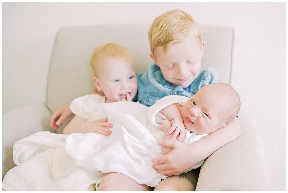 Red haired big brother and sister hold their baby brother on their lap